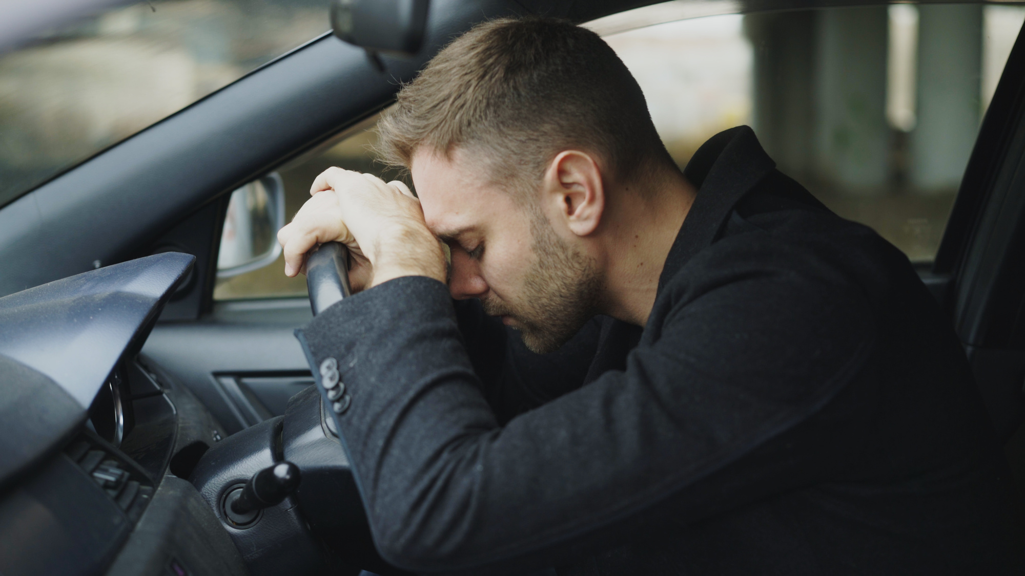 man in car with head on steering wheel