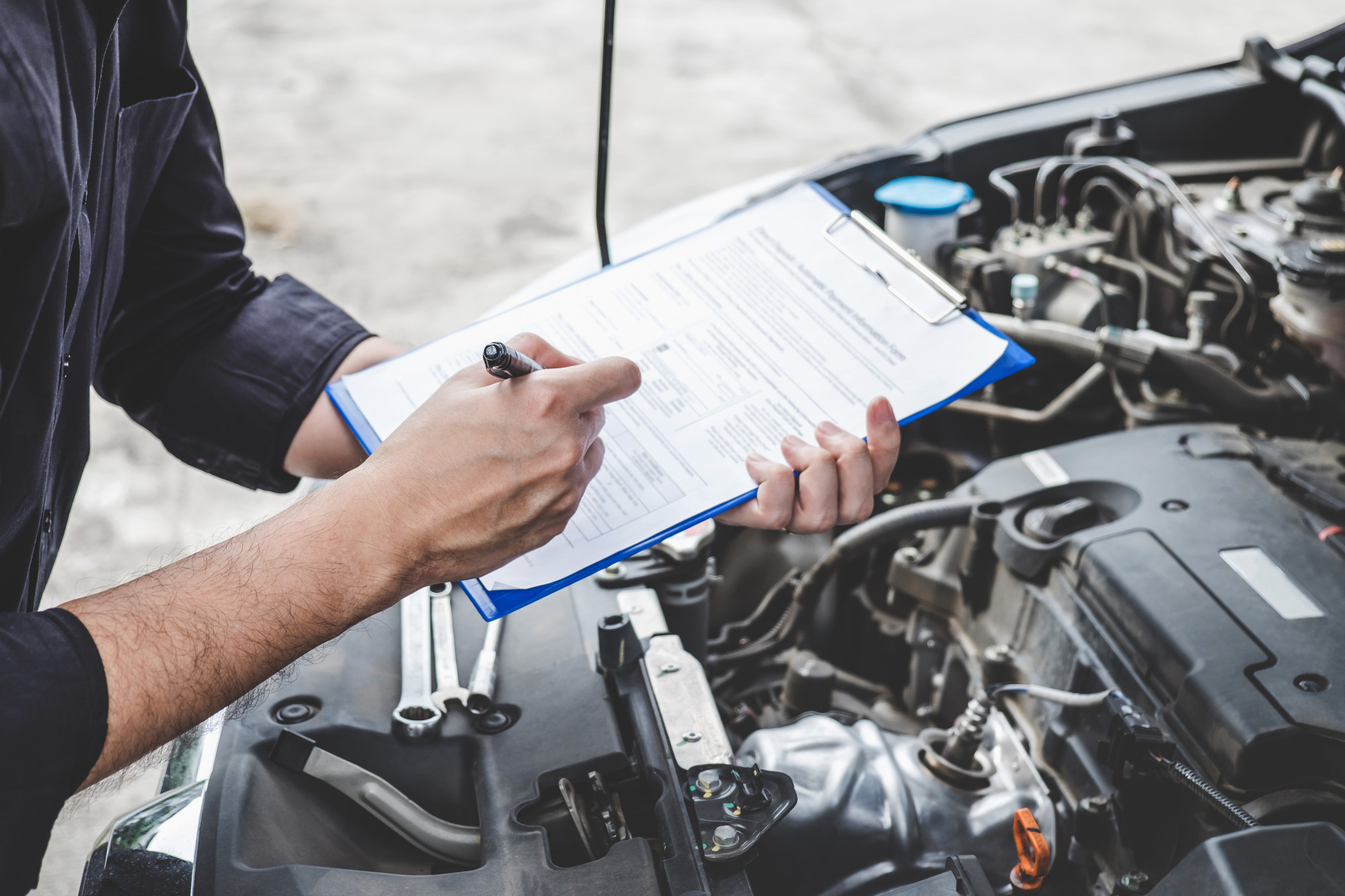 mechanic looking at car with clipboard